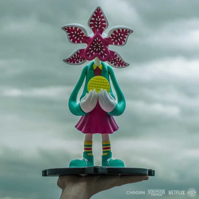 A vinyl toy sculpture of a creature. They are holding an ego waffle and have a human body, but a five-pronged flower-like head with teeth.