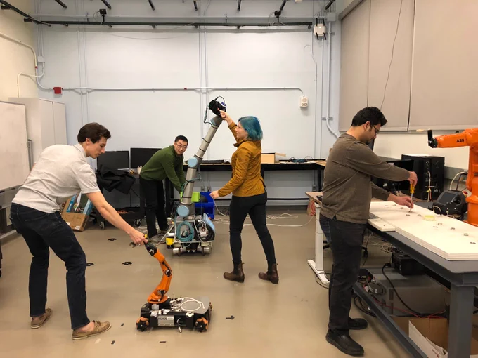Four MIT PhD students each paired with a different robot, seemingly interacting with these robots in some abstract manner. 