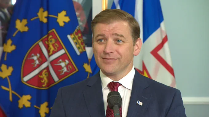 Andrew Furey stands in front of the provincial flags and a microphone.