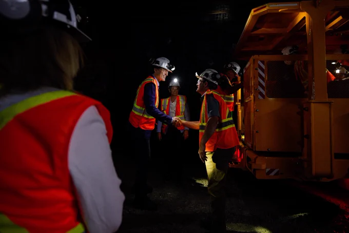 Prime Minister Justin Trudeau is standing in a mine and shaking hands with an employee. In the foreground and background, other people are also visible.