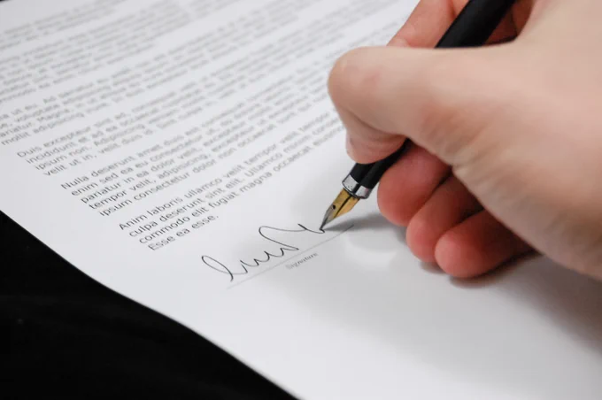 A hand holding a black fountain pen signing a typed document.