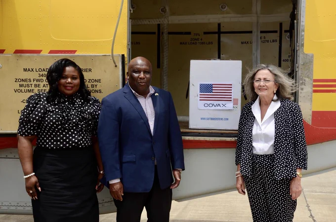 Two women and one man pose in front of an open delivery truck. Inside the truck is a white box labeled with an American flag and the word COVAX. 