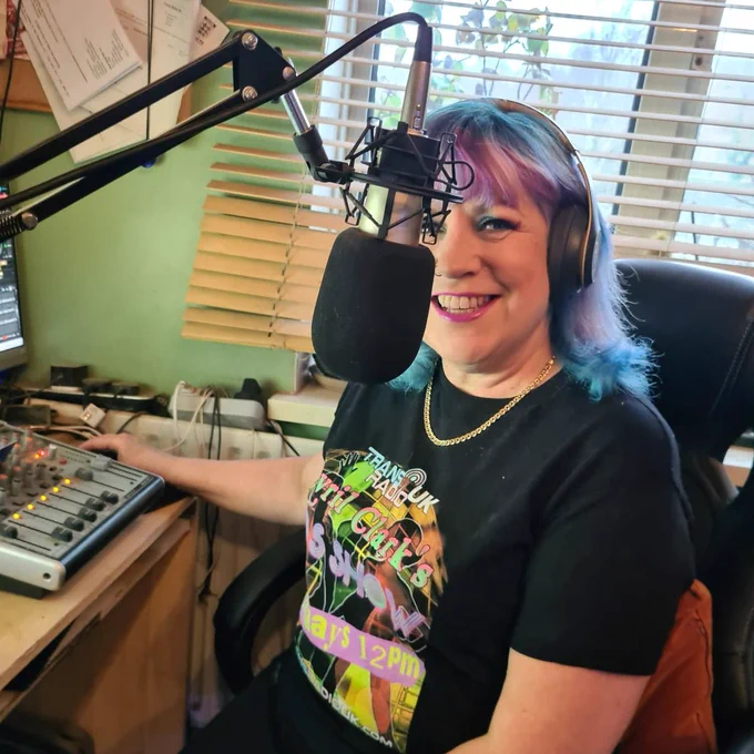 Picture of Avril sitting in the studio in front of a mixer and mic on a stand. She is smiling at the camera and is wearing headphones.