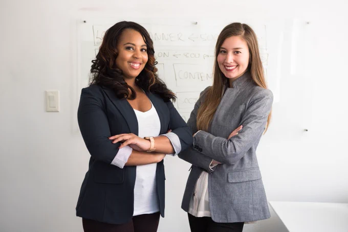 Two female executives stand together in front of a whiteboard