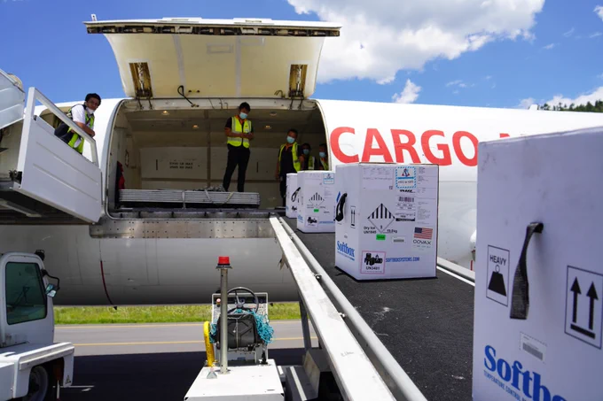 Airport crew members use a baggage conveyor to unload boxes of COVID-19 vaccines from the cargo bay of an aircraft.