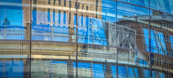 The facade of the Finnish parliament reflected in the window of the Finnish Parliament Annex building.