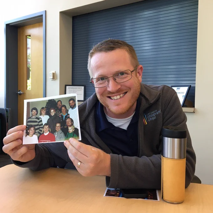 Man smiling, holding childhood photo
