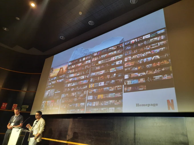 Two speakers at podium with slide showing the Netflix homepage