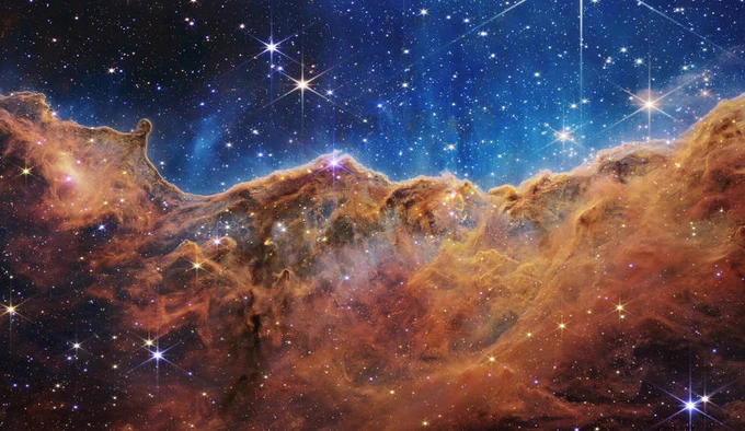 This landscape of “mountains” and “valleys” speckled with glittering stars is actually the edge of a nearby, young, star-forming region called NGC 3324 in the Carina Nebula. Captured in infrared light by NASA’s new James Webb Space Telescope, this image reveals for the first time previously invisible areas of star birth. Credits: NASA, ESA, CSA, and STScI
