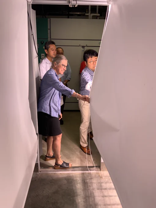 A woman holds a canvas barrier open as a man looks into what's behind the curtain.