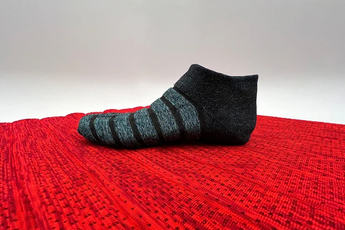 A black and gray ankle sock on a red mat.