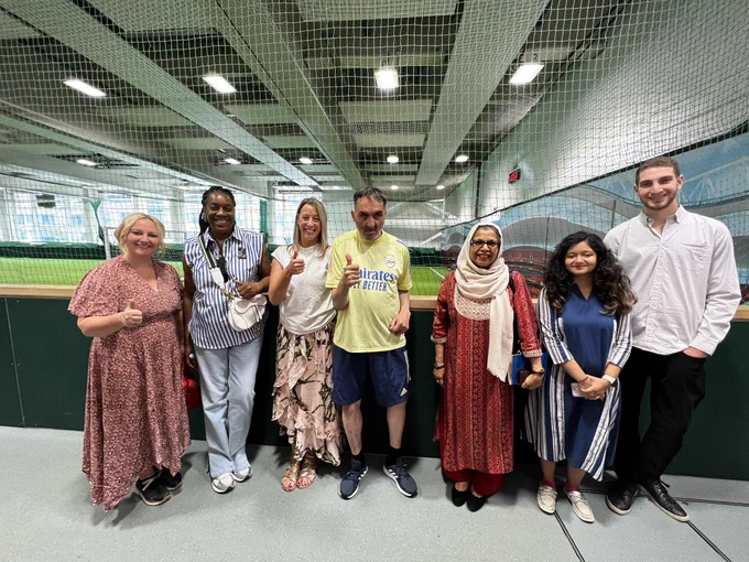 This is a photo of seven individuals standing outside an indoor football pitch with their thumbs up.