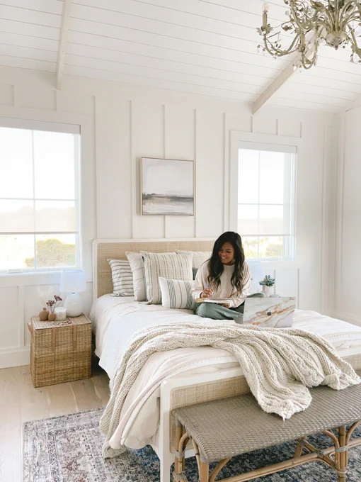 Lifestyle blogger Nina Williams is sitting on her bed and there are classic solar shades covering her windows.
