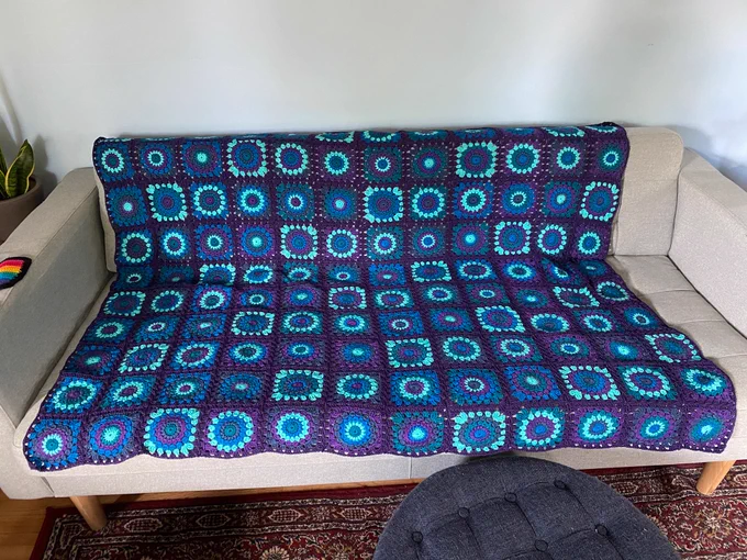 A blue, green, indigo, purple, mint blanket of sunburst crocheted circles. Organized in a 10x12 grid. 