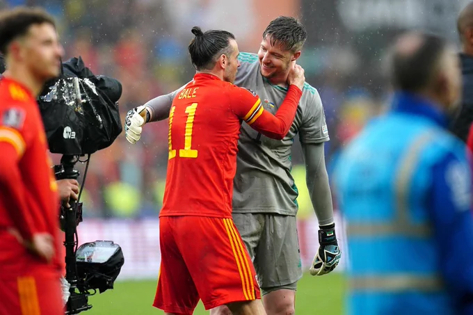 Wayne Hennessey, Cymru goalkeeper is moving to embrace his teammate and great friend, Gareth Bale. A light rain falls from the heavens.

Hennessey, wearing his grey goalkeeper strip and huge gloves is smiling broadly as he stretches out his long right arm to wrap around his pal. 

Bale, in the red of Cymru with yellow detailing on his sleeves and shorts, has his right arm and hand raised to Hennessey's shoulder and neck – a warm, celebratory gesture as he moves in for the embrace. Bale's surname is seen in typography across his shoulders, while a large 11 covers much of his upper back – denoting his favoured squad number. 

In the foreground, just out of focus on the left of the photograph, their teammate Ethan Ampadu looks on. Directly behind Ampadu, although masked somewhat by the player, is a cameraman supporting a steadicam – the camera, shrouded in a wet weather cover, is trained on the Hennessey-Bale embrace.

Is is, truly, a bromance for the ages.