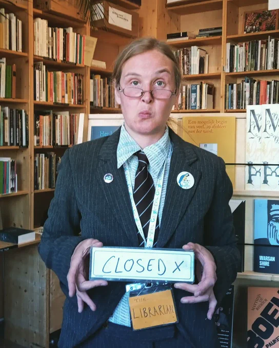 The Itinerant Poetry Librarian holding The Library "CLOSED" sign