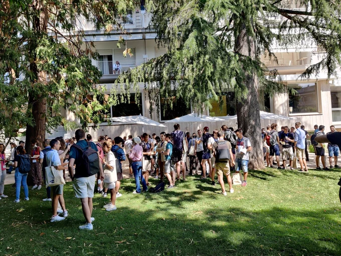 A coffee break at ACACES 2022 with people standing on the grass between trees outside the Hotel Silva Splendid