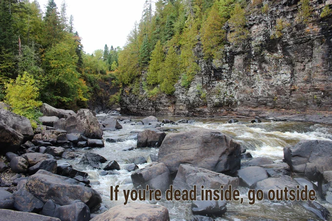 River flowing through tree lined rocky cliffs with text overlay "if you're dead inside, go outside"