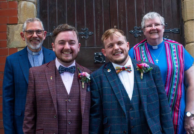 A newly married couple stand in front of two Methodist ministers and a Methodist church.
