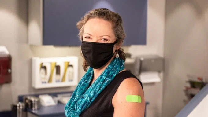 Person sitting in a doctor’s office with a green bandage on their arm.