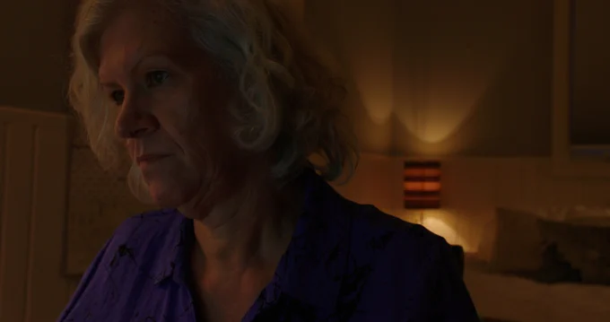 Quilter Marilyn Farquhar sits looking at something off screen - that appears to bring bad news. 