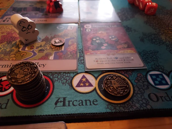 A photo of the boardgame 'Oath', focused on a section of the board with a stack of coins in the Discord house, and a card: 'Gambling Hall'