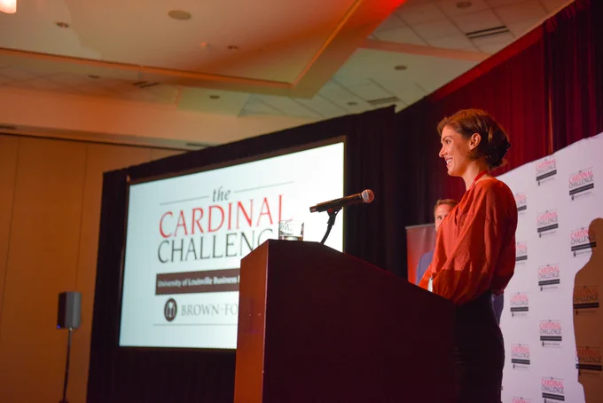 Student standing at podium with a Cardinal Challenge sign. 