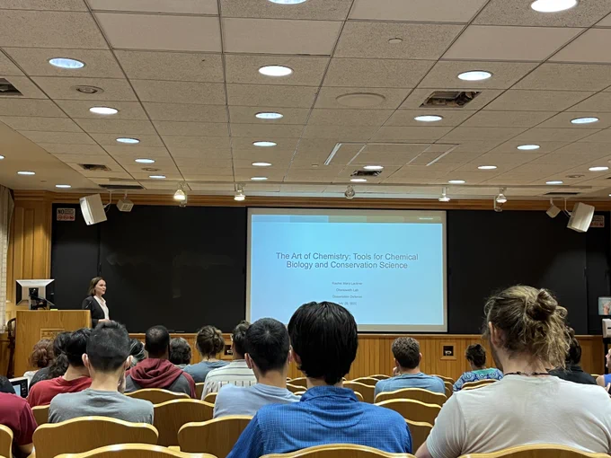 A lecture hall with people looking at a slide entitled "The Art of Chemistry: Tools for Chemical Biology and Conservation Science." 