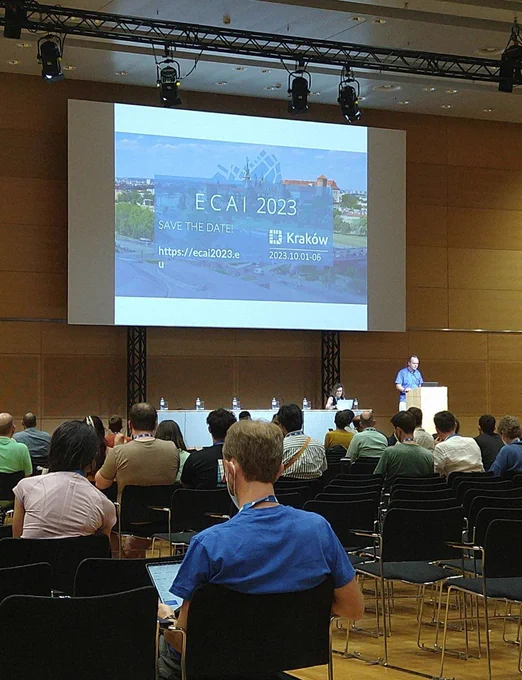 ECAI 2023 organizers announce ECAI 2023 at IJCAI-ECAI 2022 with slide in background that reads ECAI 2023, Kraków 2023.10.01-06 save the date https://ecai2023.eu 