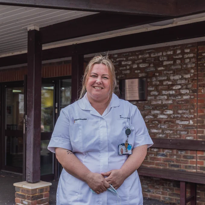 Woman wearing blue nurses uniform, looking and smiling at the camera.