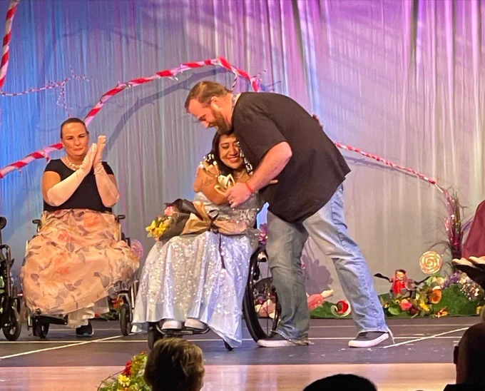 Brad, wearing jeans and a black shirt, hugs Erica Myron, Ms. Wheelchair USA 2021, while accepting his award.