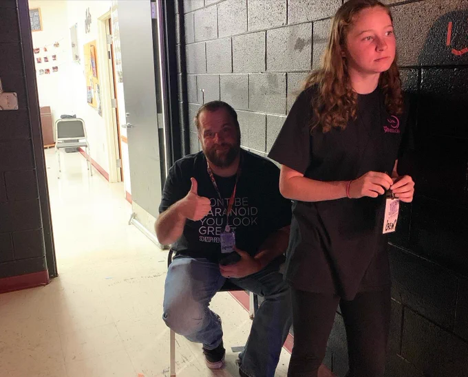 Brad sits back stage and gives a thumbs up as he hides behind stage crew so his wife cannot see him while she is competing in Ms. Wheelchair USA 2022.