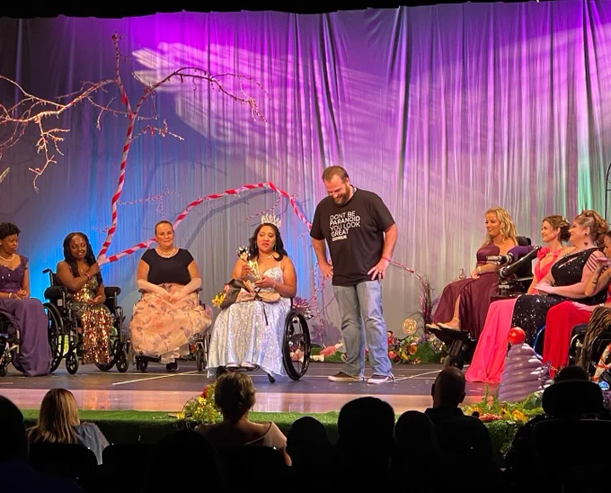 Brad stands on stage with the 2022 Ms. Wheelchair USA contestants as he is being presented his award.