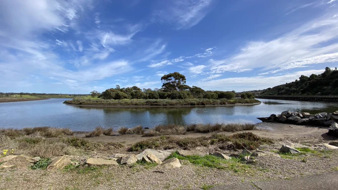 A horseshoe bend of river under a blue sky streaked with white clouds