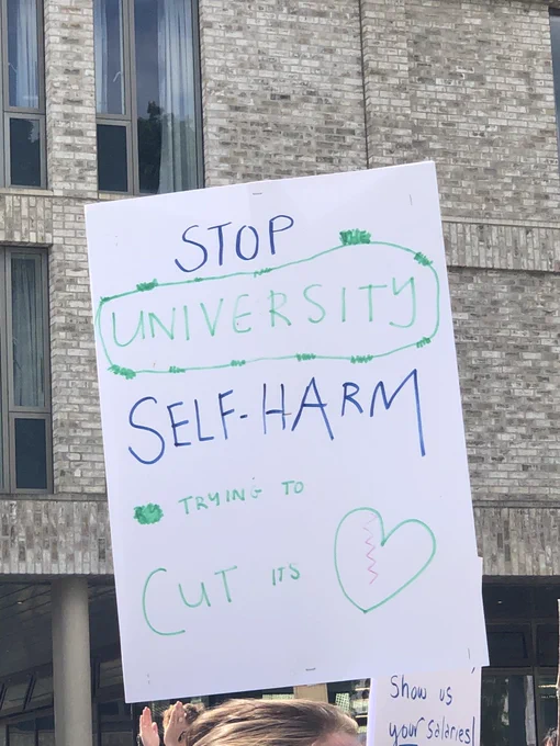 Protest sign that reads ‘stop university self-harm trying to cut its heart’. In place of the word heart is a green broken heart.