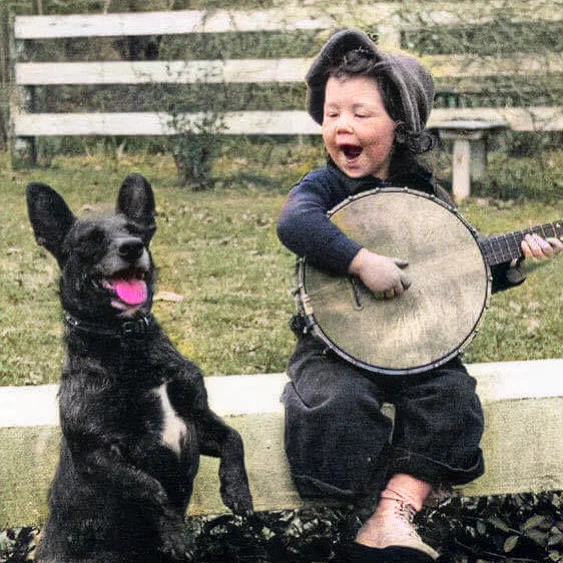 A young boy playing the banjo with his dog, 1920. Colorize