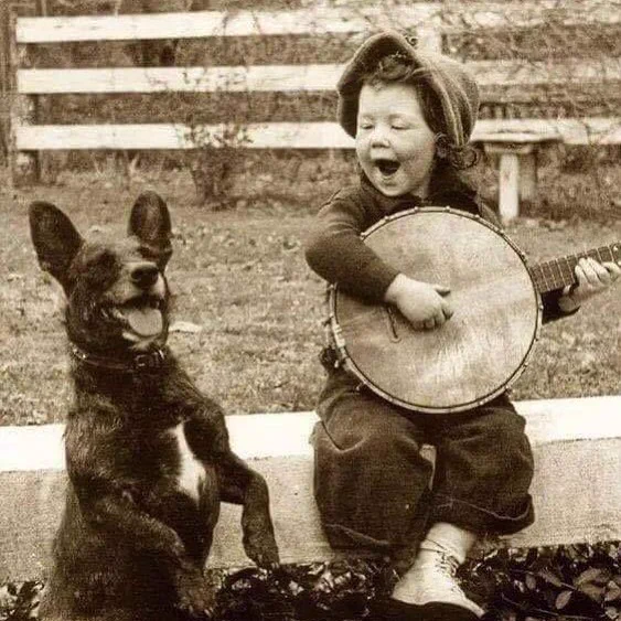 A young boy playing the banjo with his dog, 1920. B/W