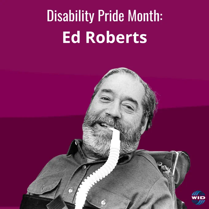 Ed Roberts smiles with his respiratory tube in his mouth while sitting in his wheelchair.