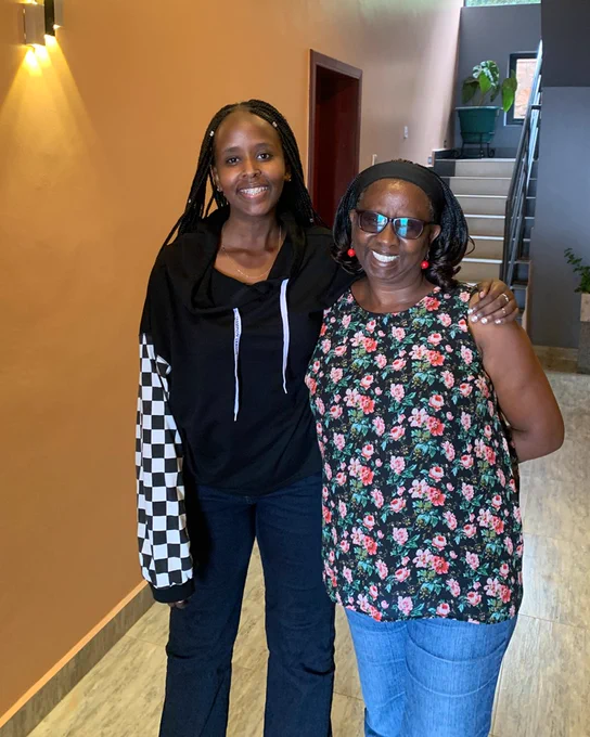 Angela wearing a black jacket with checkered sleeves, smiling with her arm around a woman in a floral shirt.
