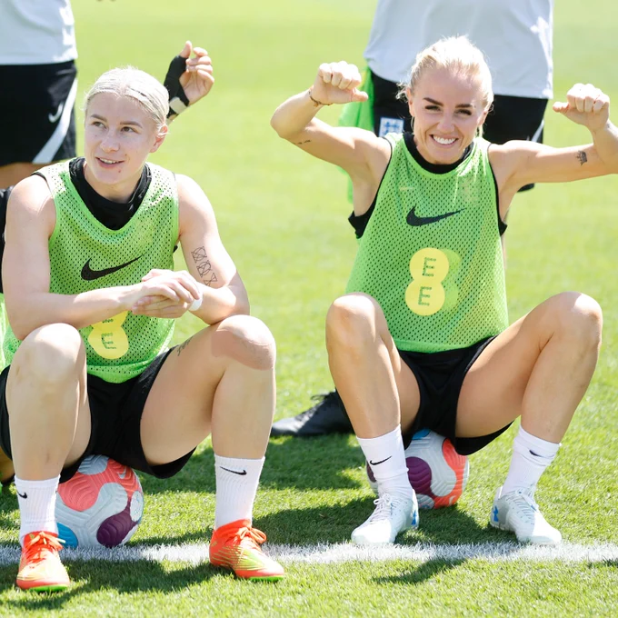 Bethany England and Alex Greenwood sitting on footballs at training, celebrating winning the challenge,