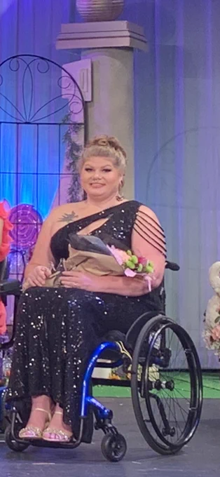 Ashley pictured in her wheelchair wearing a black gown holding her award and flowers
