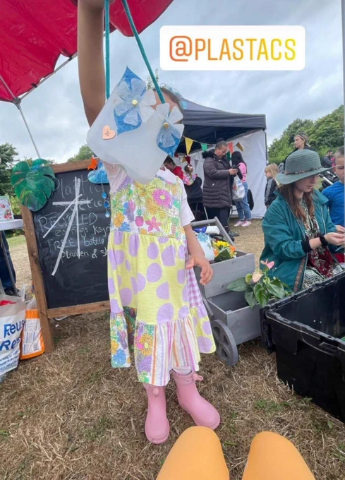 Milk bottle planter, decorated with stickers and cut out leaves and flowers, 
being held up by a small child (obscuring her face)