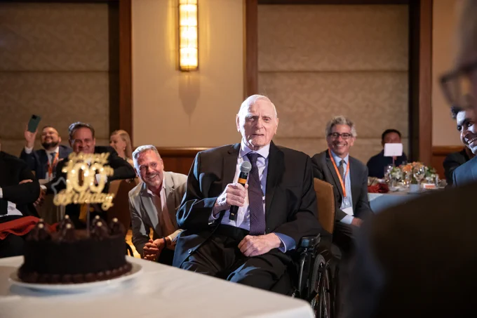 Professor John B. Goodenough holds a microphone as he as honored at a dinner for his 100th birthday.