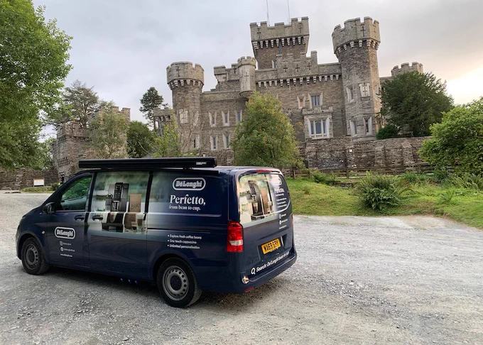 A De'Longhi coffee van is parked in front of a large castle.