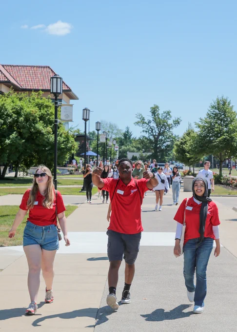 A large group of people smile and pose for a photograph while walking outside.