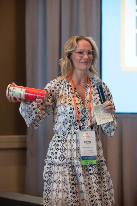 Mallory Willsea with what could be deemed either a look of curiosity, confusion, or frustration holding a dented can of Pringles. and wearing a traditional conference lanyard with a name badge.