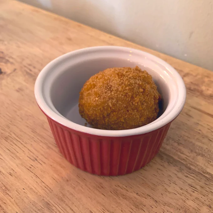 A little vegan scotch egg in a red and white ceramic cup. The background is a wooden table.