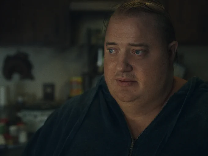 A close-up of Brendan Fraser with a thin comb-over, wearing a large blue zip-up hoody and no undershirt in the film The Whale.
