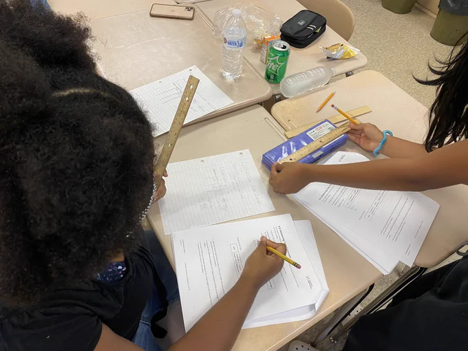 Students measuring a pencil box with a ruler.