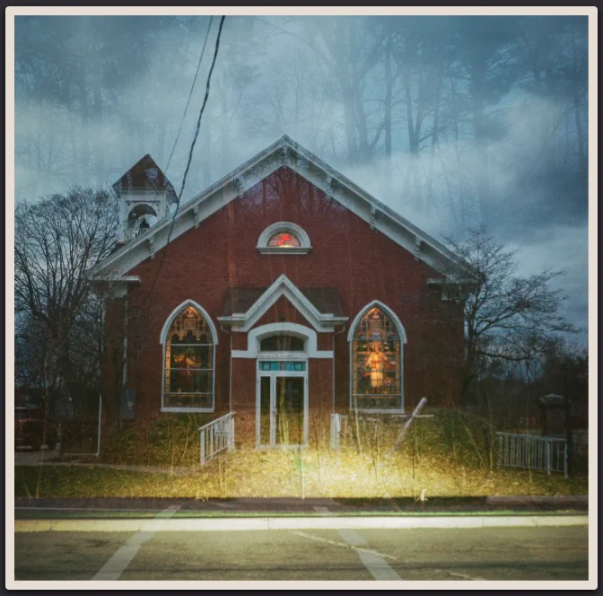 A double exposure of the church Kate. attended as a child overlaid with the woods of a rest area. The church is red brick with white trim around it's windows and roofline. The stained glass windows flanking the door are illuminated. The sky above the church is gray. Overlaid on the clouds are the tops of the trees of the rest area. Below the church appears the parking stripes of a parking lot, terminating in the leaf-covered floor of the woods near the rest area.